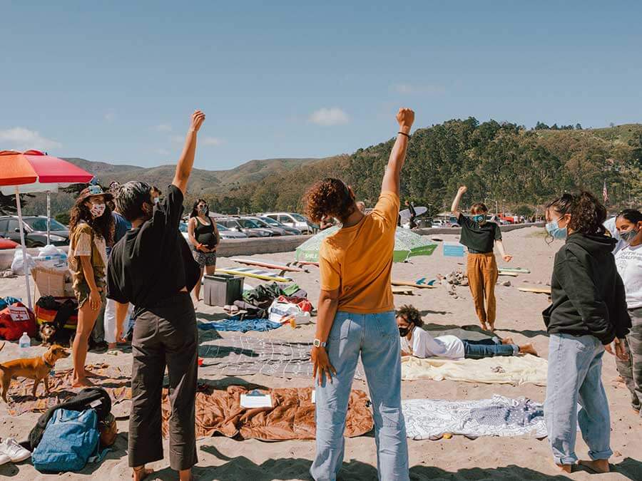 brown girl surfers gather in a circle on the beach with their fists raised
