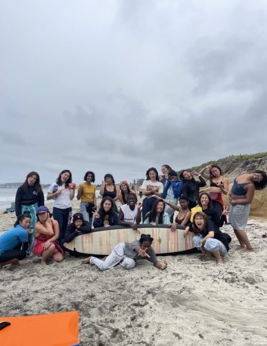 participants gather around a surfboard on the beach